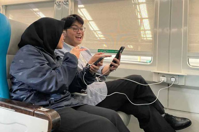Dua penumpang sedang memanfaatkan stop kontak di kereta api