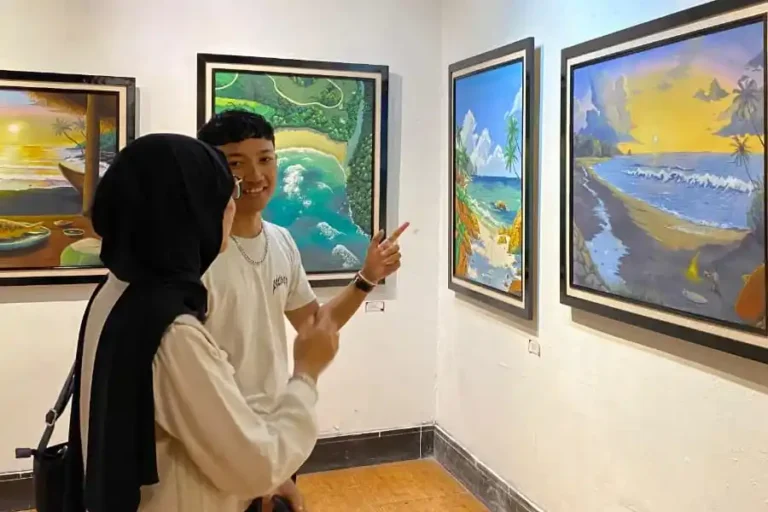 Seni Lupa, Wujud Emosional Delapan Mahasiswa UM di Galeri Raos Dimas (kanan) saat menjelaskan makna lukisannya yang bertajuk "Footprint in paradise" kepada salah satu pengunjung pameran "Seni Lupa" di Galeri Raos, Batu, Senin (10/11/25) (foto: Dok Pribadi)